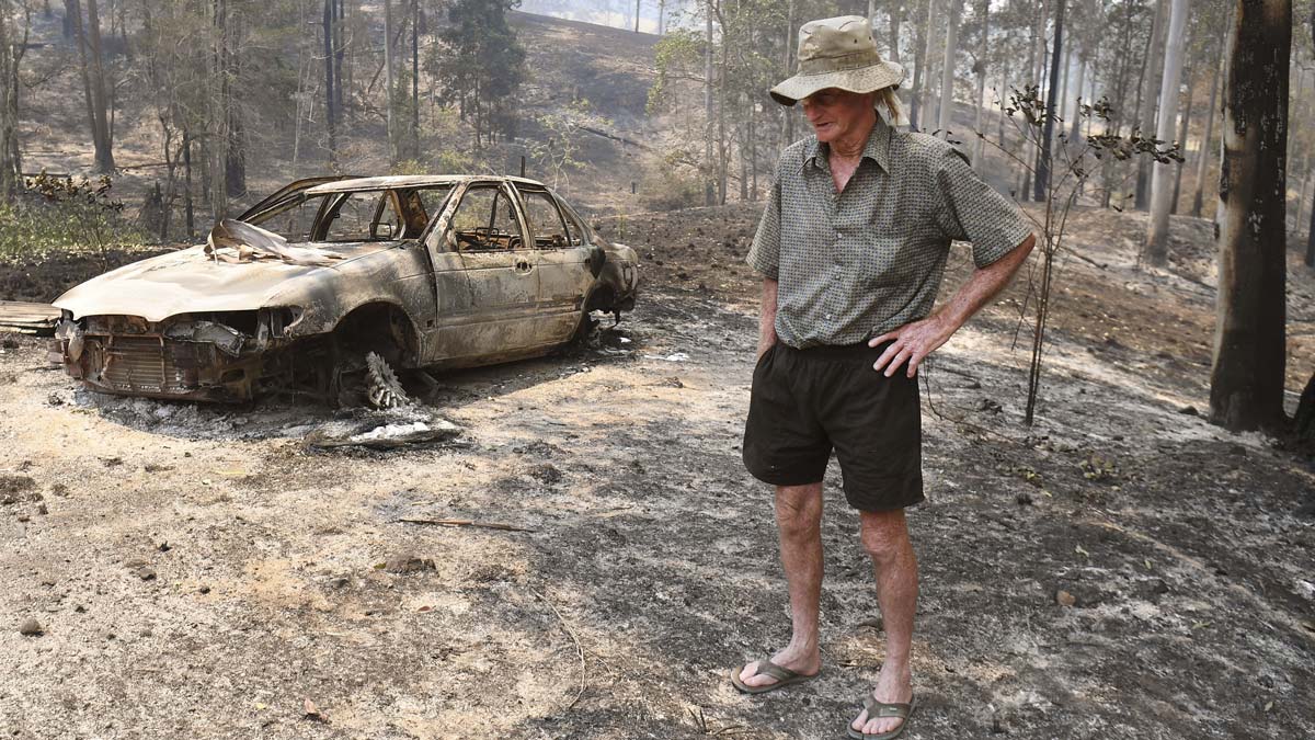 An elderly an inspects damage next to his house after bushfires