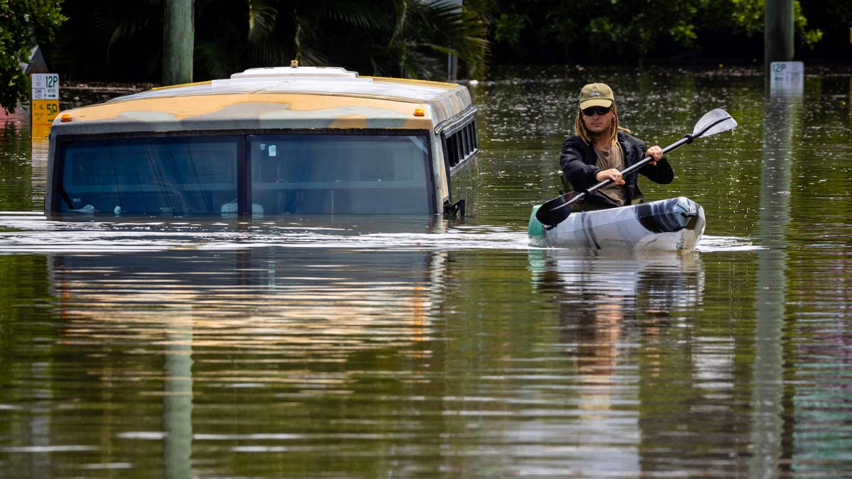 A man paddles his kayak next to a submerged bus on a flooded street